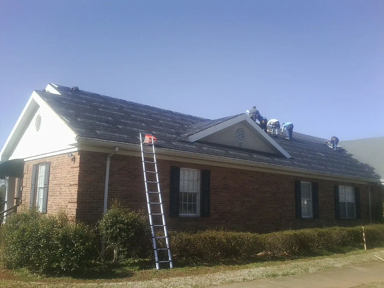 Crew tearing shingles off a brick ranch roof with a ladder set — Emergency Roof Repair work by our crew in Glen Ellyn