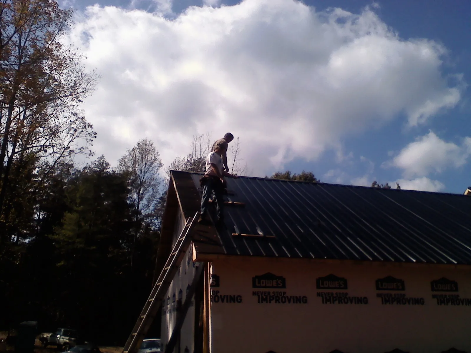 Roofer fastening dark metal panels high against a cloudy sky, from a Roof Inspection job in Glen Ellyn
