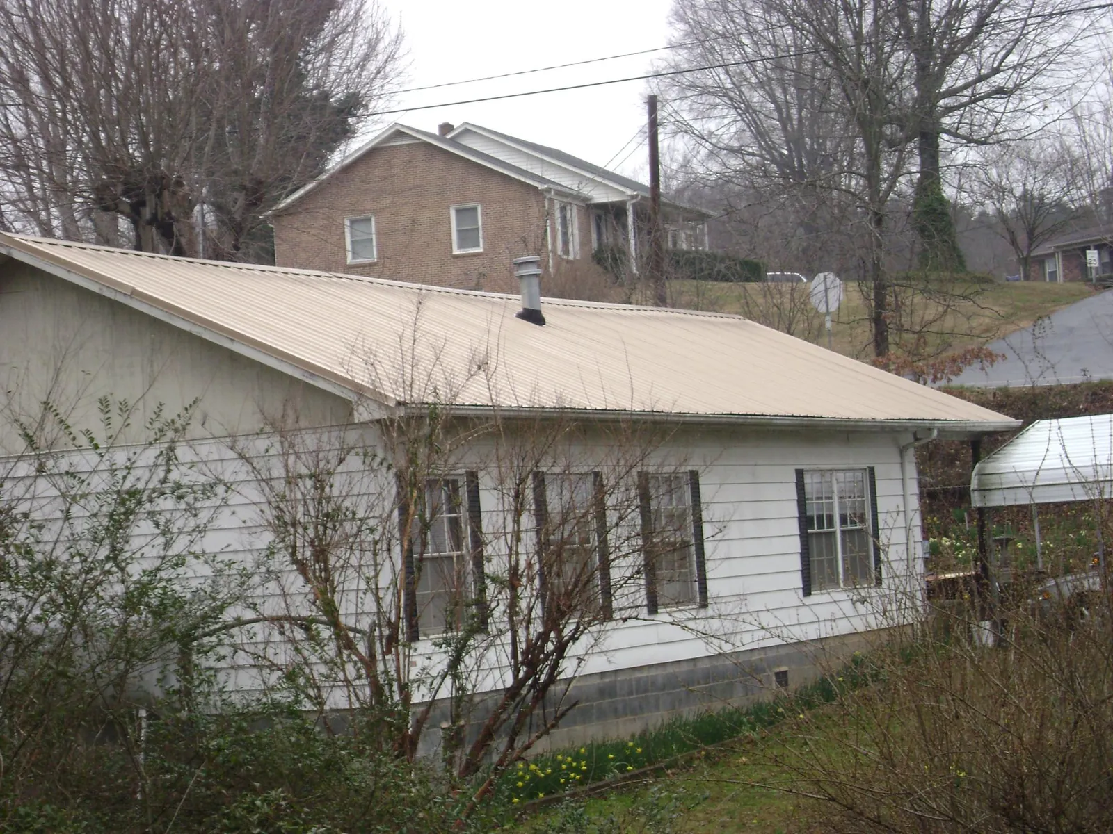 Tan metal roof on a white sided house set into a hillside — Commercial Roofing by Roofing Brothers in Glen Ellyn